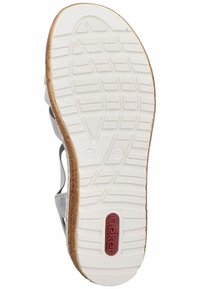 Semelle de sandale blanche avec un motif en caoutchouc texturé, présentant une bordure marron et un logo rouge. Design flexible avec des côtés découpés pour une meilleure respirabilité.
