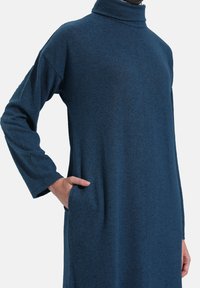 Abito a maniche lunghe con colletto alto, realizzato in tessuto blu scuro texturizzato, dotato di tasche laterali e vestibilità comoda.