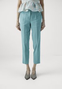 Vaaleansiniset pellavahousut, joissa on muotoleikkaus, kapenevat lahkeet ja sivuplektra, yhdistettynä harmaisiin korkokenkiin, joissa on terävä kärki.