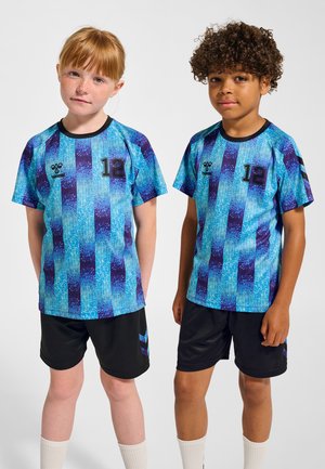 Två barn bär matchande fotbollströjor med kort ärm. Tröjorna är blå med ett mönster av vertikala ränder i olika nyanser av blått och lila. Varje tröja har numret "12" och en logotyp på framsidan. De kombineras med svarta shorts och vita strumpor.