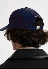Blå corduroy baseball cap med en buet skygge; har justerbar rem og broderet detalje på bagsiden; textured overflade.