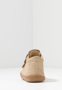 Hellbraune Schuhe aus strukturiertem Material, mit niedrigem Absatz, runder Zehenpartie und einer geschnürten Akzentuierung hinten. Gummisohle sichtbar.