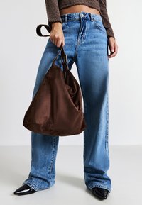Braune Wildleder-Schultertasche mit einem lässigen Design, kombiniert mit hellblauen weit geschnittenen Jeans und schwarzen spitzen Absätzen. Weiche Textur, schlichte Akzente.