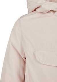 Veste imperméable rose clair avec capuche, texture lisse et poche poitrine avec un rabat arrondi. Détails de coutures visibles.