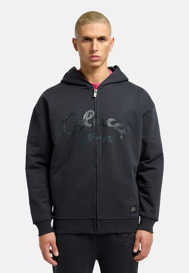 Sort zip-up hoodie lavet af blødt materiale, med hætte, ribbede manchetter og et dekorativt logo i skinnende detaljer foran.