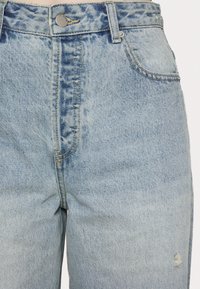 Jeans de ganga azul claro com uma cintura alta, design de cinco bolsos, costura visível e um detalhe desgastado no joelho direito.