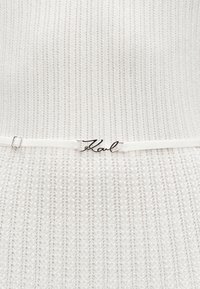 Λευκό πλεκτό φόρεμα με υφασμάτινο σχέδιο και λεπτή ζώνη με ασημί διακοσμητικό λογότυπο "Karl". Το ύφασμα έχει κάθετες ριγέ λεπτομέρειες.