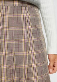 Falda de cuadros con patrones en marrón, amarillo y rosa, con diseño plisado y tejido texturizado. Mostrada con una manga de suéter gris.