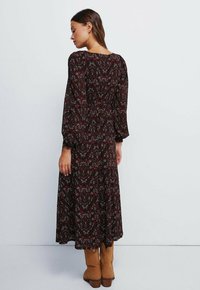 Černé a červené vzorované maxi šaty s dlouhým rukávem, s přiléhavým korzetem a splývavou sukní, s kulatým výstřihem a měkkou texturou látky.