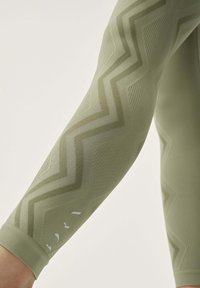 Green patterned leggings featuring a zigzag design and ribbed texture. Accents include small white marks near the hem.