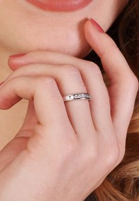 Silberring mit geradem Design, verziert mit fünf kleinen klaren Steinen entlang des Bandes, getragen an einer Hand mit natürlichem Nagellack.