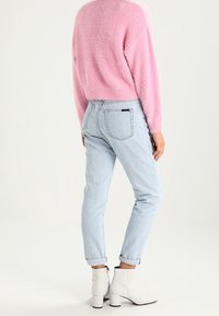 Jeans bleu clair avec une coupe fuselée, ourlets retroussés et poches arrière. Assortis à un pull rose duveteux et des bottines blanches.
