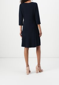 Tmavě modré šaty s rukávy do tří čtvrtin a přiléhavým pasem, s rozšířenou sukní. Nosit s světle růžovými lodičkami na podpatku.