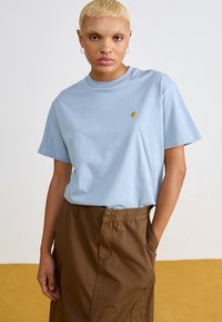 Lichtblauw katoenen T-shirt met een ronde hals en korte mouwen, voorzien van een klein geel logo op de borst, gecombineerd met bruine broek met elastische taille.