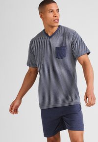 T-shirt a righe navy e bianche a maniche corte con scollo a V e taschino sul petto, abbinato a pantaloni corti navy in tessuto morbido. Design semplice e casual.