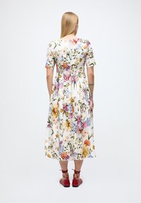 Midi-jurk met korte mouwen en bloemmotief, heeft een witte basis, meerkleurige bloemenpatronen en een getailleerde taille, gecombineerd met rode platte schoenen.