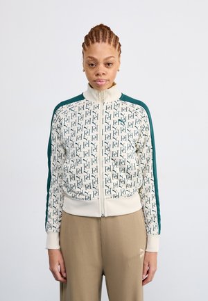 Zippered track jacket in cream with green accents, featuring a repeating logo pattern. Ribbed cuffs and hem, high collar.