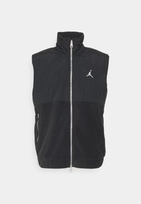 Veste noire sans manches avec col montant, zip complet à l'avant, poche zippée sur le côté et logo Jumpman blanc sur la poitrine gauche.