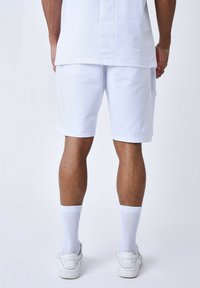 Pantalones cortos de algodón blancos con un corte recto, bolsillo lateral y detalles de costura sutil, combinados con calcetines blancos de caña corta y zapatillas deportivas blancas.