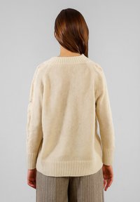 Maglione a maglia color crema con scollatura e polsini a costine. Caratterizzato da dettagli scoloriti sulle spalle. Tessuto morbido e testurizzato.