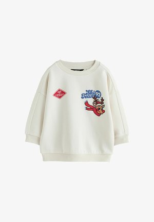 Kindersweater in crèmekleur met geribde kraag en manchetten, met een rood "North Pole Slopes" patch en een rendier met tekst "Ski Team 92".