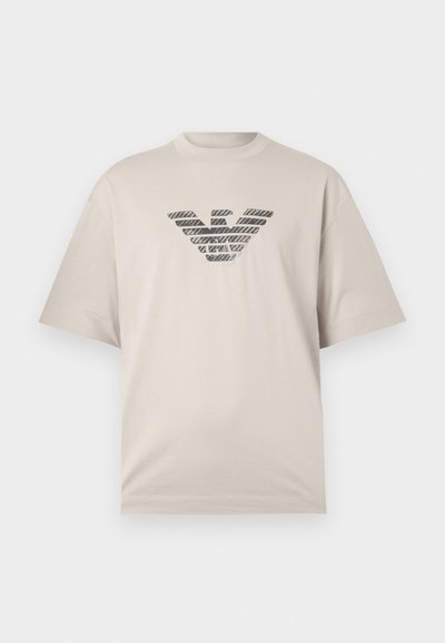 Beige bomull t-skjorte med kortermet og rund hals, med et teksturert svart logo i stripe mønster i midten.