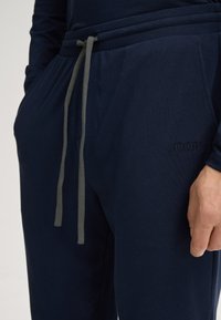 Pantaloni jogger blu navy realizzati in tessuto morbido. Presentano un cordoncino grigio, tasche laterali e un logo ricamato sul davanti.