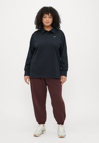 Čierna polo košeľa s dlhým rukávom a golierom, so značkou Nike, v kombinácii s vínovými teplákmi a svetlými teniskami.