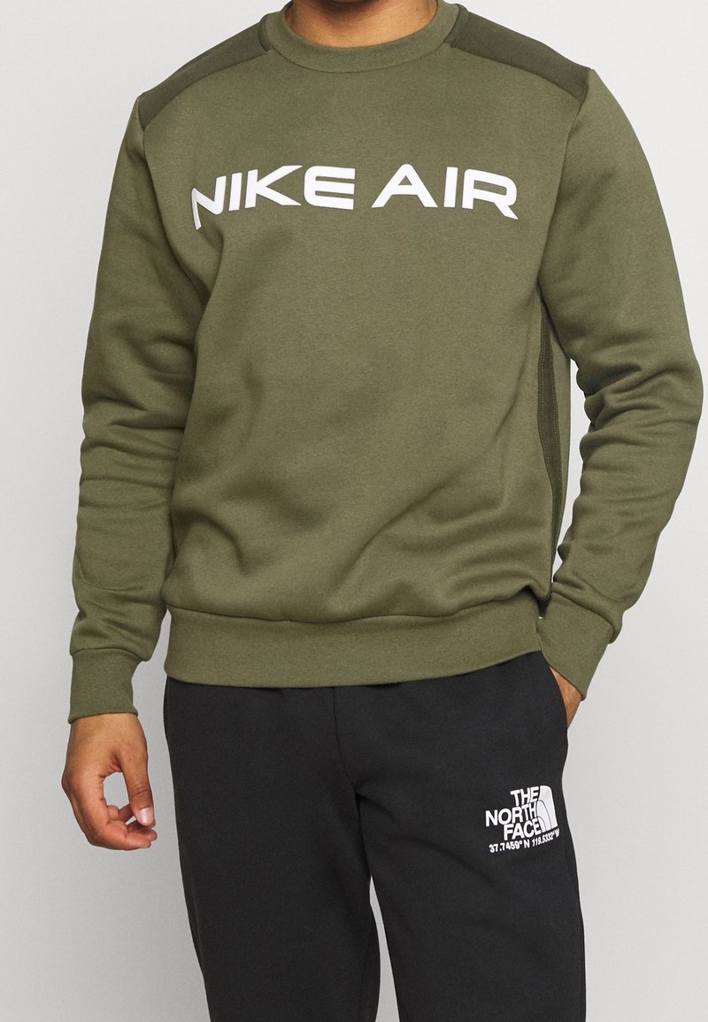 Olivově zelená mikina vyrobená z měkké látky, s kulatým výstřihem a výrazným bílým logem "NIKE AIR" na hrudi.
