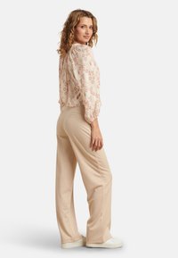 Beige, loose-fitting trousers paired with a light, patterned blouse featuring a geometric design. Model stands with a slight turn.
