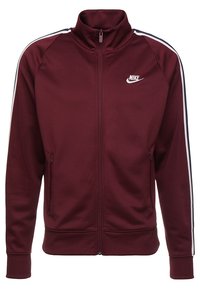 Kurtka na zamek Nike w kolorze bordowym z białymi paskami, kieszeniami na zamek, wysokim kołnierzem i logo na lewej piersi. Gładka tkanina o sportowym kroju.