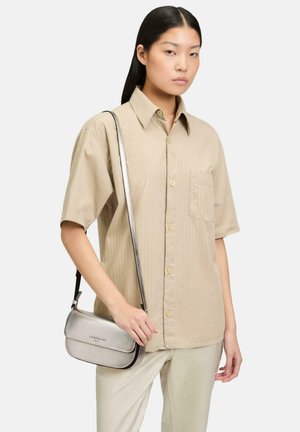 Beige gestreiftes Kurzarmhemd mit einer Brusttasche, kombiniert mit einer metallisch silbernen Umhängetasche mit Schnappverschluss und Logo-Akzent.