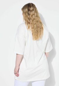 Hvid oversized kortærmet bomulds t-shirt med lige skæring, der har en glat tekstur og en længere bagkant.