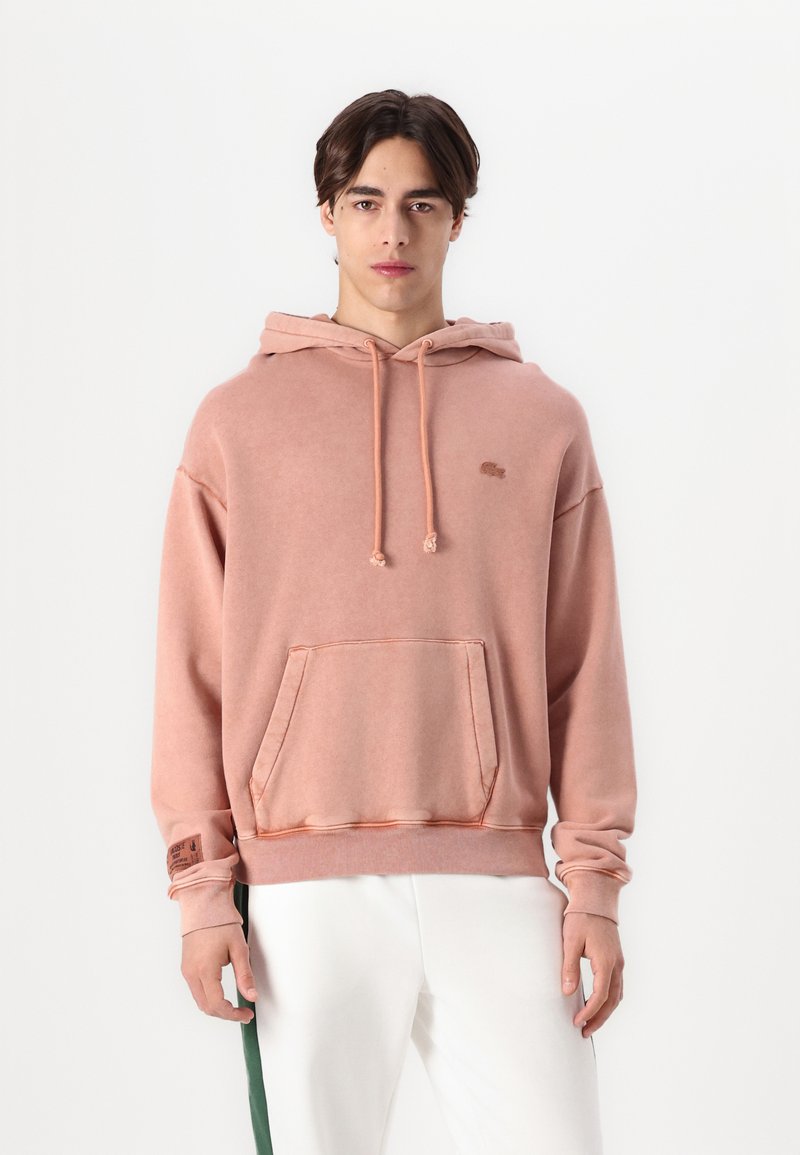 Sudadera con capucha en color rosa empolvado, hecha de suave tela de algodón. Cuenta con un bolsillo frontal, cordón ajustable y un pequeño logo en el pecho.