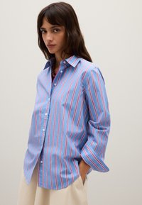 Camisa de botones azul claro con rayas verticales rosas y blancas, mangas largas con puños y un corte relajado.