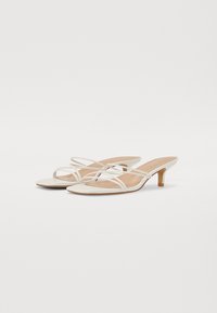 Escarpins slingback en simili cuir blanc avec des brides croisées et un petit talon effilé. Texture lisse, design minimaliste et bout ouvert.