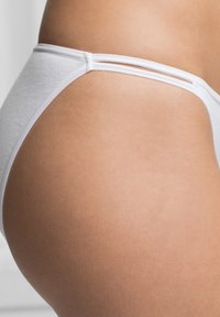 Tanga bianco in cotone con texture liscia, caratterizzato da un design minimalista e spalline strette, visto di lato.