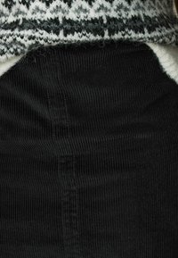 Svart sammetstyg med en ribbad textur, i kombination med en vit och svart mönstrad stickad topp som delvis syns i nederkanten.