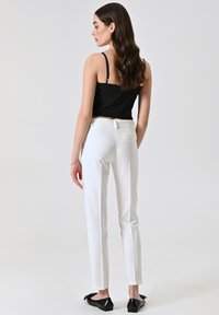 Pantalons blancs ajustés avec une coupe slim et des poches latérales, associés à un top court noir. L'ensemble présente un design épuré et un minimum de détails.