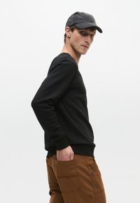 Fekete pulóver hosszú ujjakkal, bordás mandzsettákkal és kerek nyakkivágással, barna cargo nadrággal párosítva, amely több zsebbel rendelkezik.