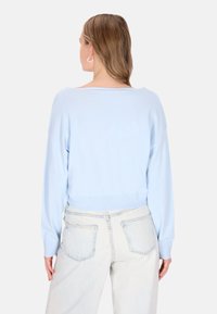 Maglione azzurro chiaro in tessuto morbido a maglia, con scollatura ampia e orlo a coste. Indossato con jeans chiari e dalla vestibilità comoda.