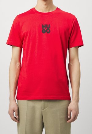 T-shirt en coton rouge avec un logo noir "HUGO" sur la poitrine. Manches courtes et col rond. Texture lisse, coupe décontractée.
