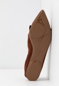 Chaussure à talons hauts en daim marron avec un bout pointu et une semelle brillante marron ornée de motifs gravés et du nom de la marque.