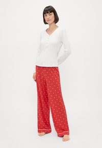 Ensemble de sommeil deux pièces comprenant un haut blanc à manches longues avec un col en V et un pantalon ample à motifs rouges avec des motifs floraux et un ourlet contrasté.