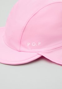 Vaaleanpunainen hattu, joka on valmistettu sileästä kankaasta ja jossa on kaareva lippa. Varustettu "P.O.P." -logolla valkoisena. Saumaompeleet näkyvät saumoissa, ja hattu on kevyttä muotoilua.