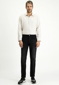 Camicia chiara a maniche lunghe con bottoni, abbinata a jeans nero attillati e sneakers nere, presenta un outfit casual.