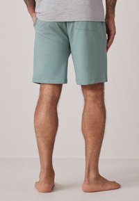 Bermudas verde menta de tejido suave, con un bolsillo trasero y un ajuste relajado, que terminan justo por encima de la rodilla. Diseño liso con dobladillos cosidos.