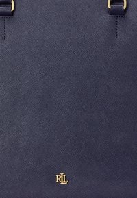 Bolso de mano texturizado en azul marino con dos asas en la parte superior y herrajes dorados. Presenta un destacado logo dorado en el centro inferior.