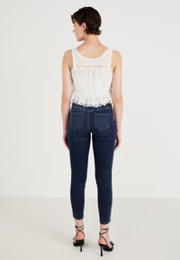 Ελαφρύ λευκό αμάνικο τοπ με δαντελένιο τελείωμα, σε συνδυασμό με στενά σκούρα μπλε τζιν και μαύρα πέδιλα με λουράκια και διακοσμητικά καρφιά.