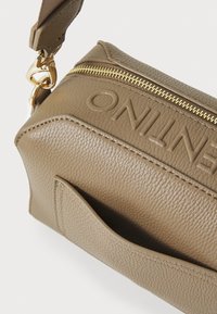 Borsa in pelle marrone con texture, dotata di cerniera dorata, marchio impresso in rilievo e tasca frontale a scomparsa. Tracolla regolabile applicata.